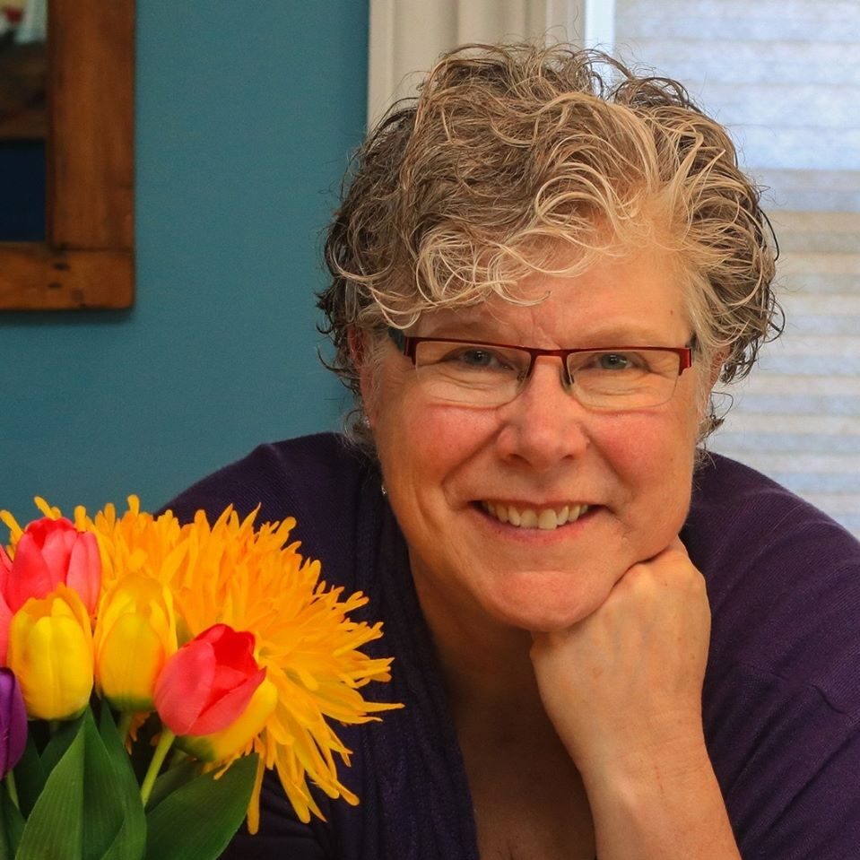 photo of woman with hand at chin, flowers at her shoulder, head shot