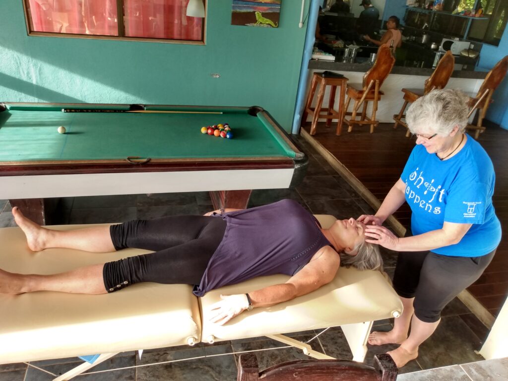 massage table with person lying on it and a facilitator holding points on the forehead, a Touch for Health balance