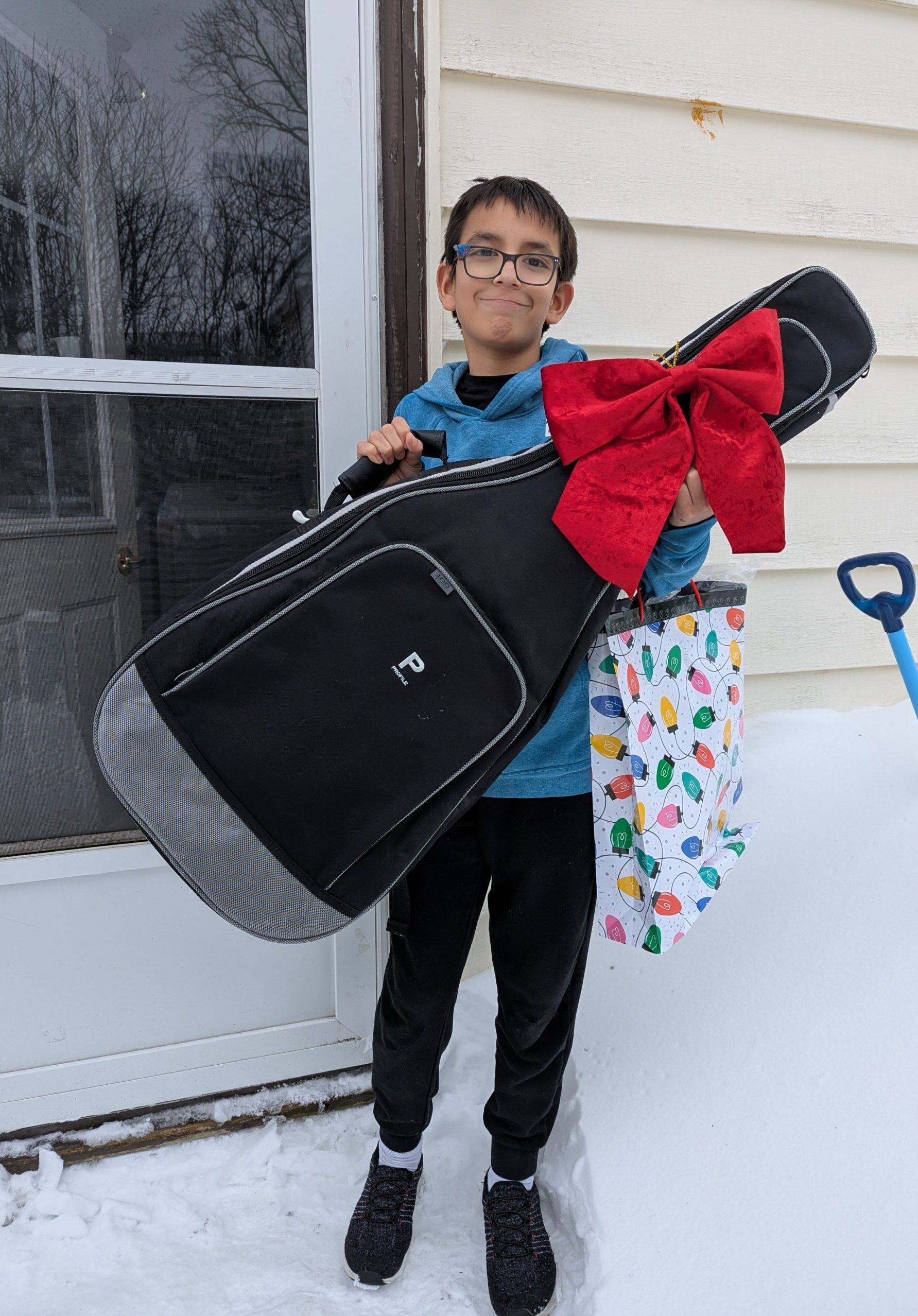 middle school boy standing on step in the snow holding guitar and gift bag
