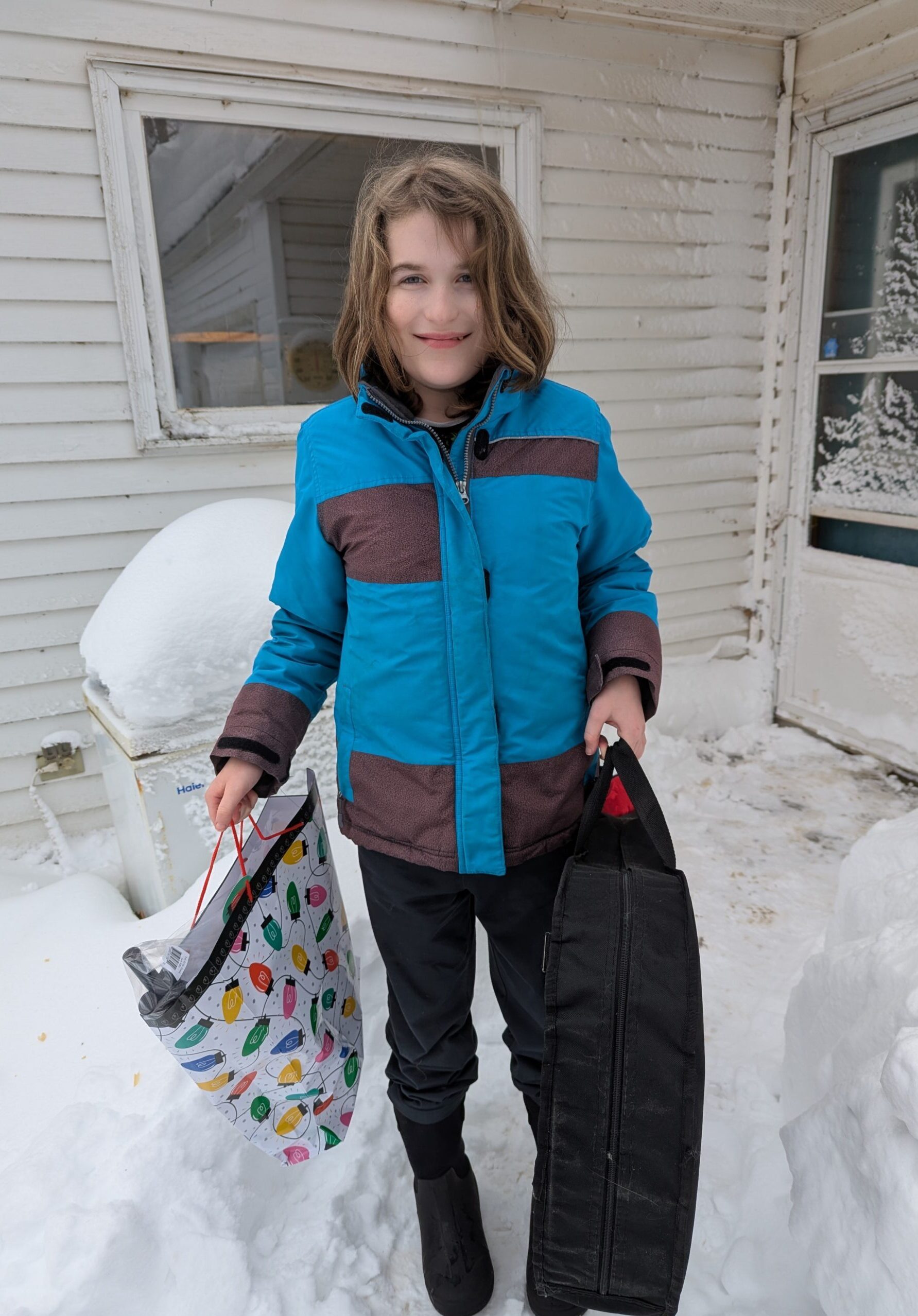 middle school student standing on front step in the snow and holding a guitar and gift bag