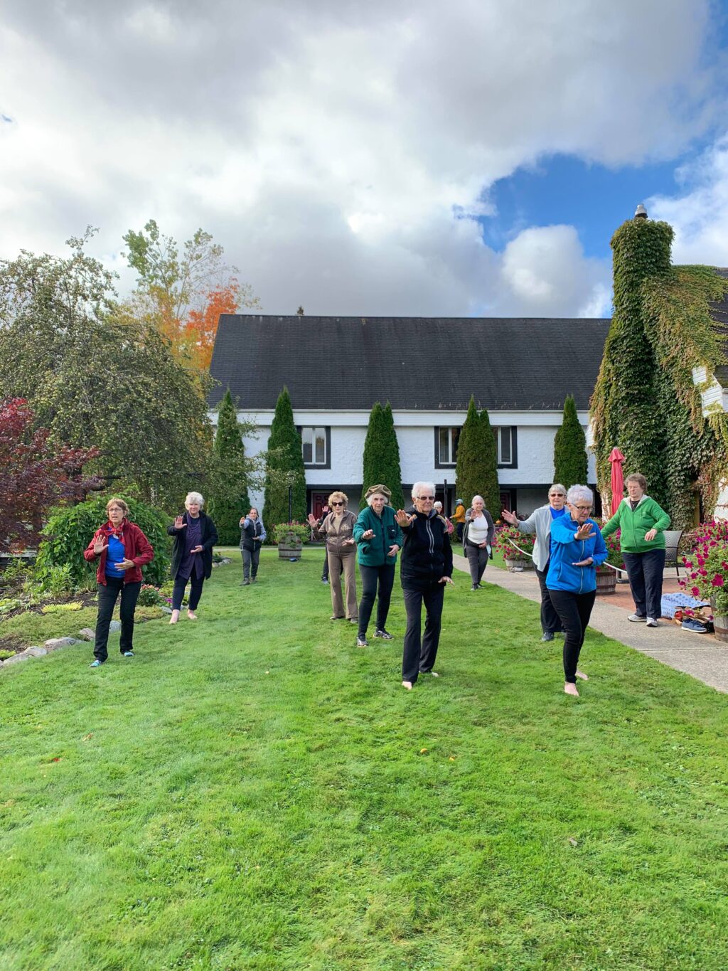 A group of people in rows doing the Tai Chi set on grass near a distillery building.