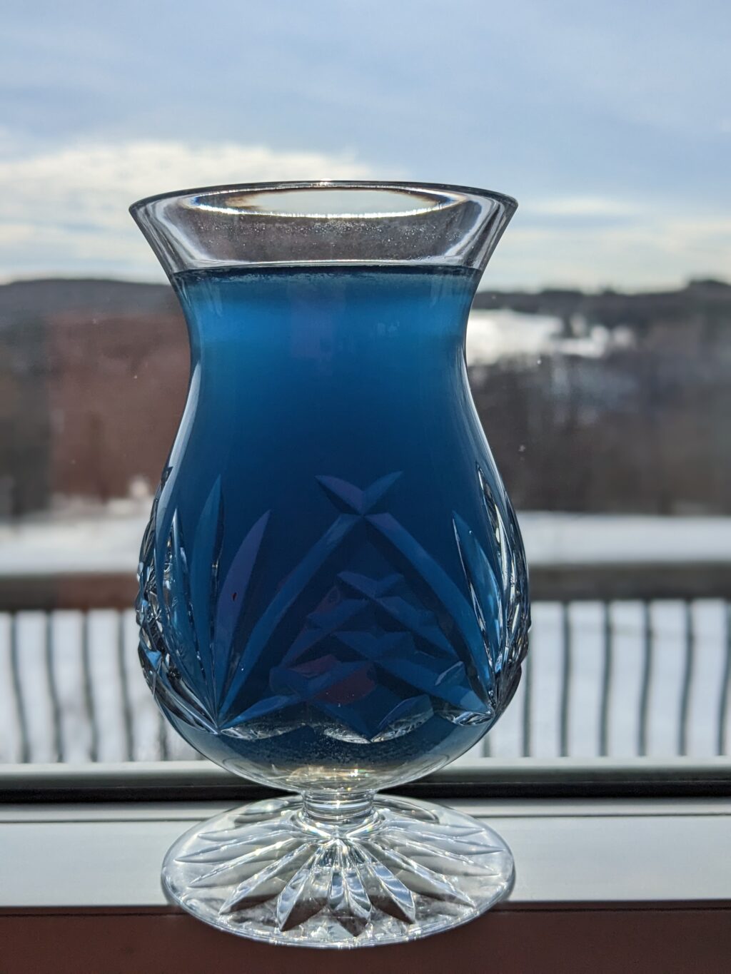 Blue matcha in a whiskey snifter on a deck railing overlooking a snowy field