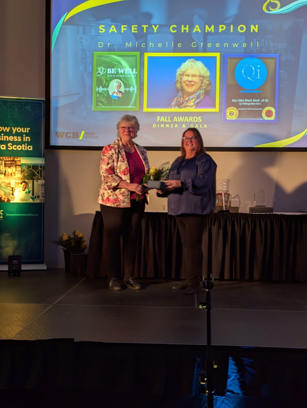 two women shaking hands and giving an award to the other on a stage