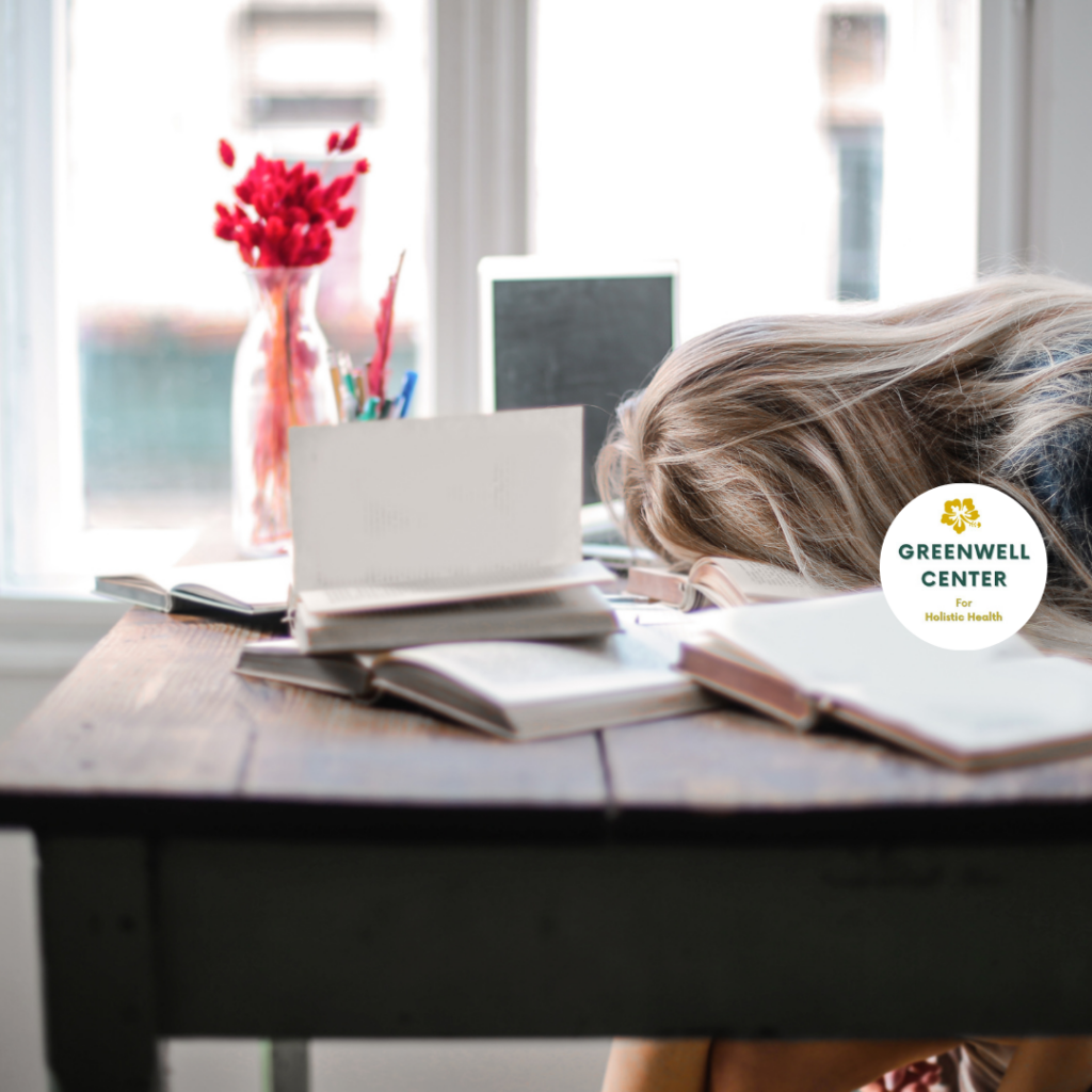 Woman with long hair with head on desk over notebooks and infront of computer