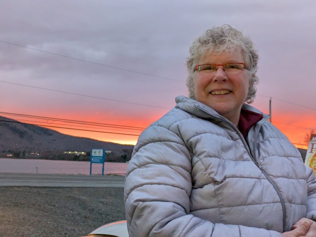 woman with shorty curly hair in ski jacket with a sunset sky behind
