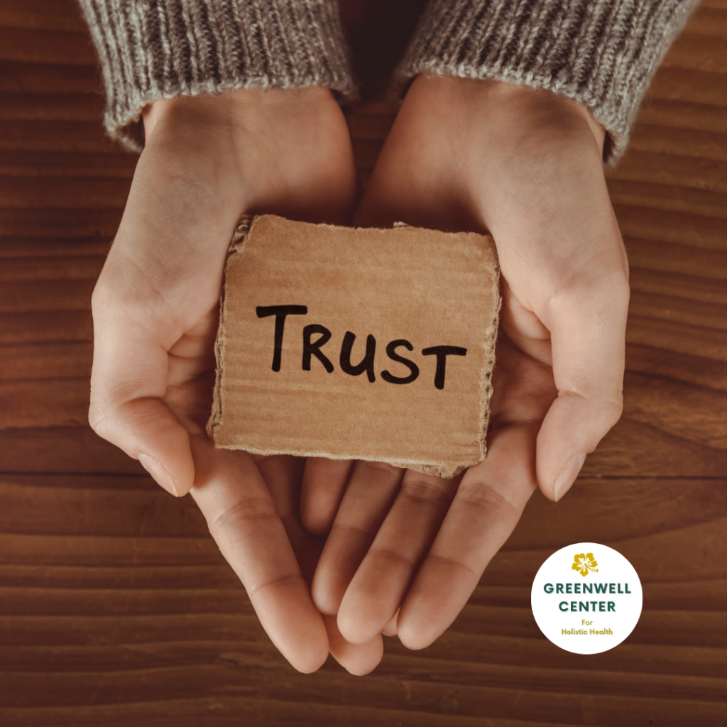 palm of hands holding a cardboard square that has trust written on it