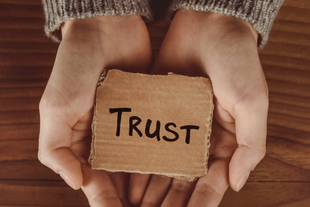 palm of hands holding a cardboard square that has trust written on it