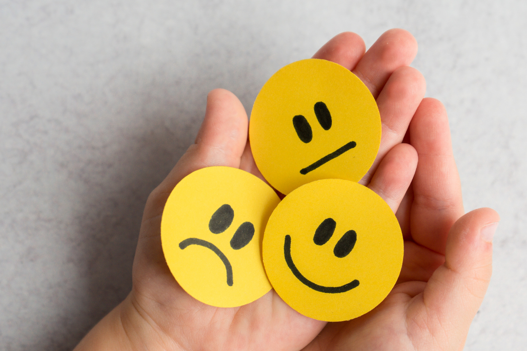 palm of hands holding 3 circles with a happy face, grumpy face and worried face